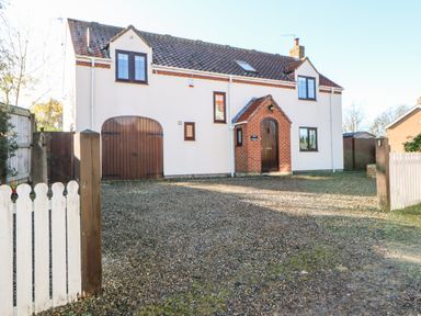 A two-story house with white walls brown roof and wooden doors with a gravel driveway at Anvil Cottage in Appleton Wiske