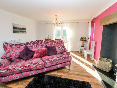 A living room with a patterned sofa a fireplace and a dining area at Anvil Cottage in Appleton Wiske