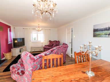 A living room with wooden dining table and chairs a silver candelabra floral sofas a television and chandeliers at Anvil Cottage in Appleton Wiske