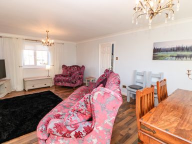 A living room with patterned sofas a wooden dining table chairs and a black rug at Anvil Cottage in Appleton Wiske