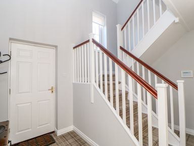 A stairway with white banisters and wooden handrails next to a white door in a hallway at Anvil Cottage in Appleton Wiske