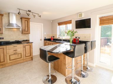 A kitchen with wooden cabinets and black countertops with three black bar stools and a granite island at Anvil Cottage in Appleton Wiske