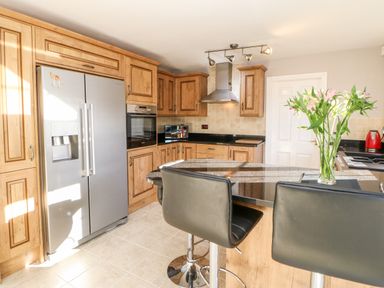 A kitchen with wooden cabinets a silver refrigerator an oven a microwave and black bar stools at Anvil Cottage in Appleton Wiske