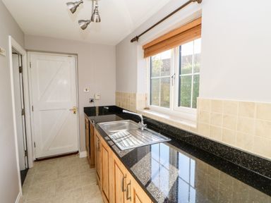 A kitchen with a sink under a window and wooden cabinets at Anvil Cottage in Appleton Wiske