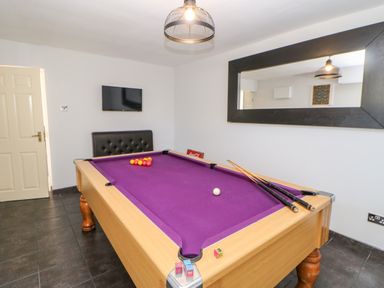 A room with a pool table with purple felt cues balls a wall-mounted television and a large mirror at Anvil Cottage in Appleton Wiske