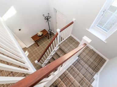 A stairway with plaid carpet leading down to a landing with a small wooden table and a coat rack at Anvil Cottage in Appleton Wiske