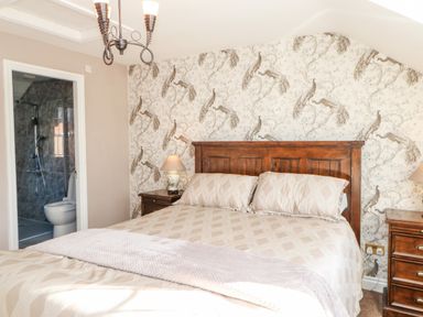 A bedroom with a double bed wooden headboard bedside tables lamps and an ensuite bathroom at Anvil Cottage in Appleton Wiske