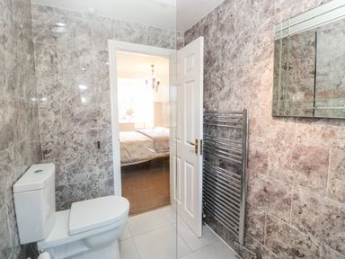 A bathroom with a toilet a heated towel rack a mirror and a door leading to a bedroom at Anvil Cottage in Appleton Wiske