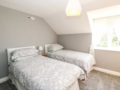 A bedroom with two single beds with floral bedding a lamp between the beds and a window with curtains at Anvil Cottage in Appleton Wiske