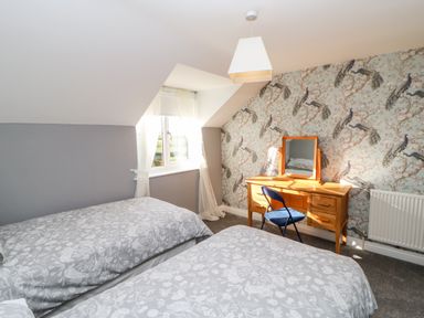 A bedroom with two single beds a wooden dressing table with mirror a blue chair and a window with curtains at Anvil Cottage in Appleton Wiske