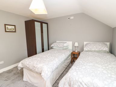 A bedroom with two single beds a wooden wardrobe and a small bedside table with a lamp at Anvil Cottage in Appleton Wiske
