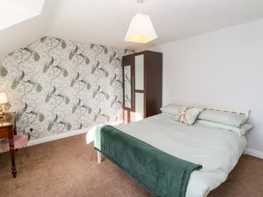 A bedroom with a bed green blanket and peacock patterned wallpaper at Anvil Cottage in Appleton Wiske