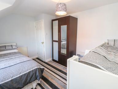 A bedroom with two single beds a wardrobe with a mirror a door and a striped carpet at Anvil Cottage in Appleton Wiske