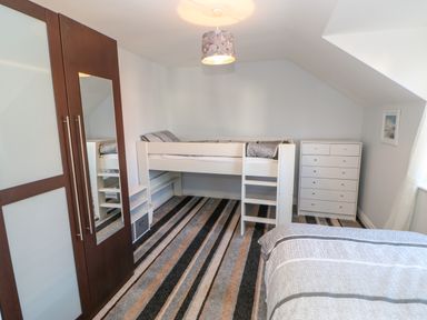 A bedroom with a white loft bed a striped carpet a dark wood wardrobe with mirror and a white chest of drawers at Anvil Cottage in Appleton Wiske