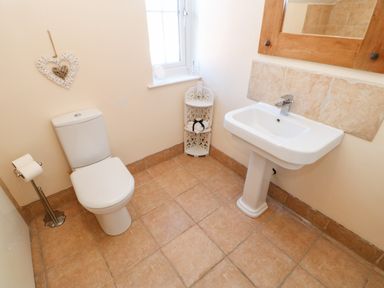 A bathroom with a toilet, a pedestal sink, a window, a corner shelf with towels, and a wall-mounted wooden mirror at Anvil Cottage in Appleton Wiske