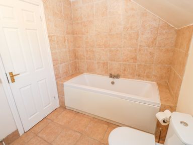 A bathroom with a bathtub next to a white door and a toilet with toilet rolls attached at Anvil Cottage in Appleton Wiske