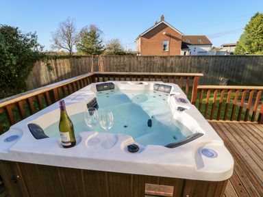 An outdoor hot tub with a bottle of wine and two wine glasses on the edge on a wooden deck at Anvil Cottage in Appleton Wiske