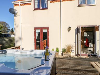 A patio with a hot tub and a bottle of wine on the edge outside a house with double doors at Anvil Cottage in Appleton Wiske