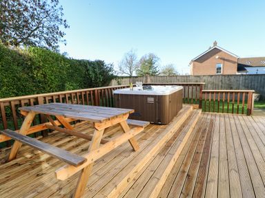 An outdoor wooden deck with a picnic table and a hot tub with glasses and a bottle at Anvil Cottage in Appleton Wiske