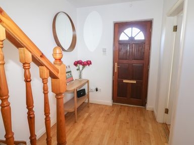 An entrance hallway with a wooden staircase a wooden table with flowers a round wall mirror and a wooden front door at 1 Closheen Lane Rosscarbery County Cork
