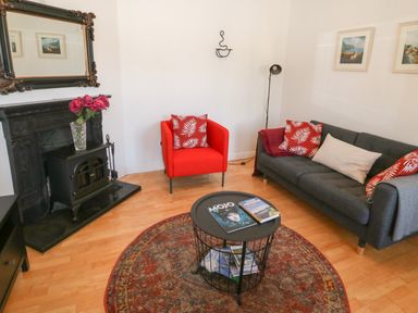 A living room with a gray sofa and red chair with patterned cushions a round coffee table and a fireplace at 1 Closheen Lane Rosscarbery County Cork