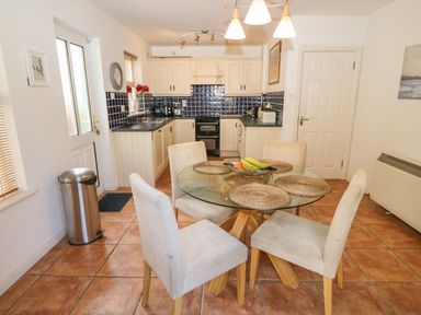A kitchen and dining area with a round glass table and four chairs a door a trash bin and tiled floor at 1 Closheen Lane in Rosscarbery County Cork