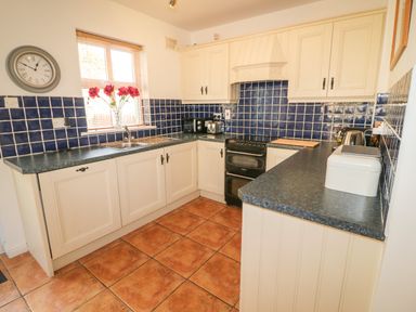 A kitchen with cream cabinets blue tiled backsplash black stove and countertop with a vase of red flowers on the window sill at 1 Closheen Lane Rosscarbery County Cork