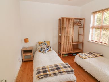 A bedroom with two single beds each with folded blankets a bedside table with a lamp and a wooden shelving unit with hangers by a window at 1 Closheen Lane Rosscarbery County Cork