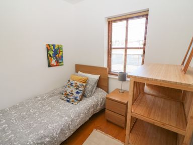 A single bed with patterned bedding and pillows next to a wooden nightstand and a window with blinds in a small bedroom at 1 Closheen Lane in Rosscarbery County Cork