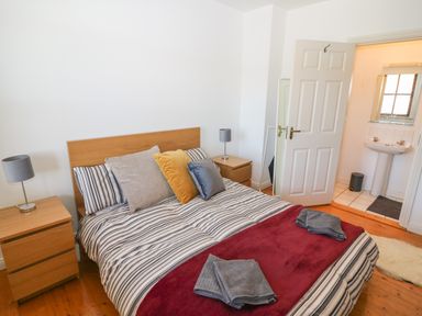 A bedroom with a bed featuring striped bedding and multiple pillows bedside tables with lamps and an open door leading to a bathroom at 1 Closheen Lane in Rosscarbery County Cork