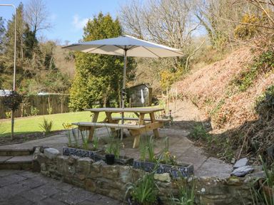 An outdoor patio area with a wooden picnic table and umbrella surrounded by plants and trees at 1 Closheen Lane in Rosscarbery County Cork