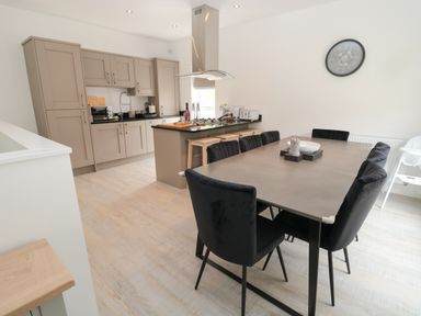 A kitchen with beige cabinets a black countertop an island with stools and a dining table with black chairs at Summer Rose in Craster
