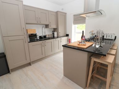 A kitchen with gray cabinets black countertops a breakfast bar with stools and kitchen utensils at Summer Rose in Craster