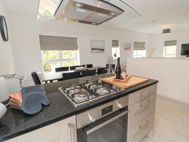 A kitchen island with a gas stove and oven alongside a dining area with a table and chairs at Summer Rose in Craster