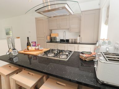 A kitchen with a black countertop island featuring a gas stove toaster and kitchen utensils at Summer Rose in Craster