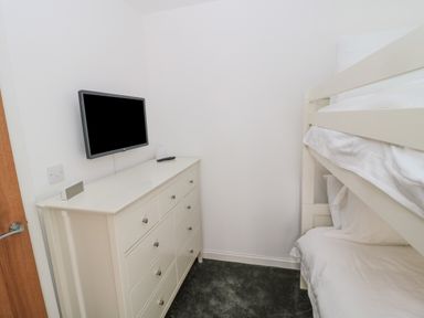 A small bedroom with a bunk bed a white dresser and a wall mounted television at Summer Rose in Craster