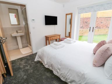A bedroom with a double bed towels on the bed a wall-mounted tv a wooden desk a full-length mirror and a door leading to a bathroom at Summer Rose in Craster