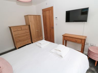 A bedroom with a bed and folded towels a wooden cabinet a chest of drawers a wooden table and a wall mounted TV at Summer Rose in Craster