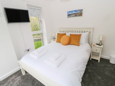 A bedroom with a bed with orange cushions white towels two bedside tables lamps a wall-mounted TV and a window at Summer Rose in Craster