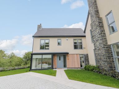 A modern two-story house with large windows a front door and a paved pathway surrounded by grass at Summer Rose in Craster
