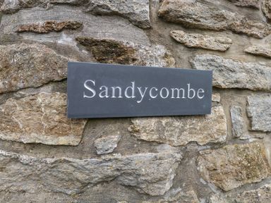 A sign reading Sandycombe mounted on a stone wall at Sandy Combe in West Bay