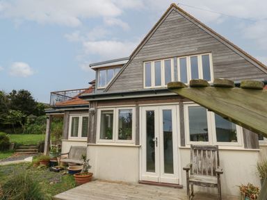 Exterior view of a two-story house with wooden and cream walls and garden furniture at Sandy Combe in West Bay