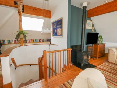 A living area with a wood stove a television a wooden stair railing and books on shelves at Sandy Combe in West Bay