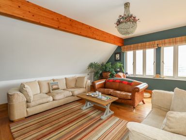 A sitting room with beige and brown sofas a wooden coffee table striped rug large windows and a chandelier at Sandy Combe in West Bay