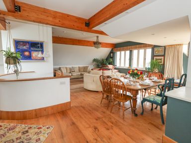 An open plan living and dining area with a wooden dining table set for a meal and beige sofas in the seating area at Sandy Combe in West Bay