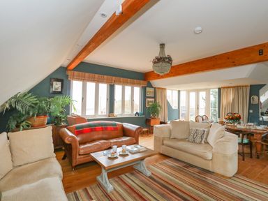 A living room with beige and brown sofas a wooden coffee table plants and a dining area with a table and chairs at Sandy Combe in West Bay