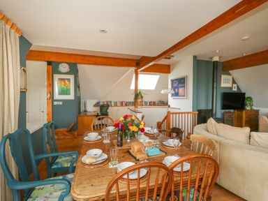 A dining area with a wooden table set for six next to a living room with beige sofas and a TV at Sandy Combe in West Bay