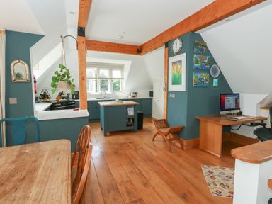 A kitchen with blue cabinets a wooden island and dining table and a small workspace with a computer at Sandy Combe in West Bay