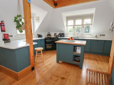 A kitchen with blue cabinets wooden flooring an island with fruit and a wooden stool at Sandy Combe in West Bay
