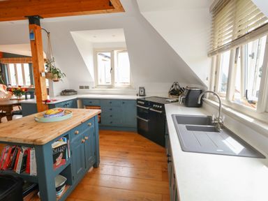 A kitchen with blue cabinets a wooden island with books and fruit a black stove a gray sink and windows with blinds at Sandy Combe in West Bay